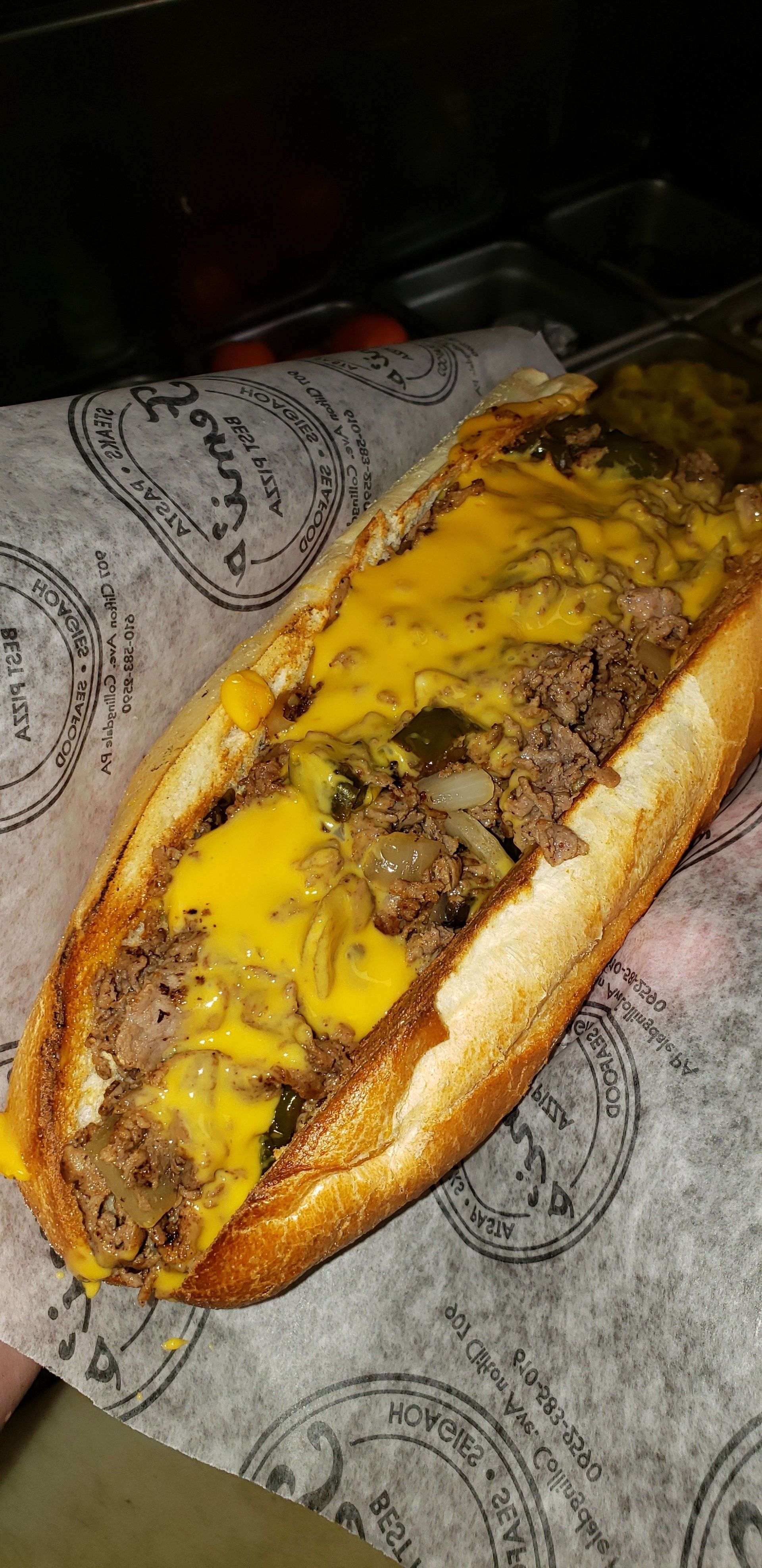 A steak sandwich with cheese and onions on a bun is sitting on a piece of paper.