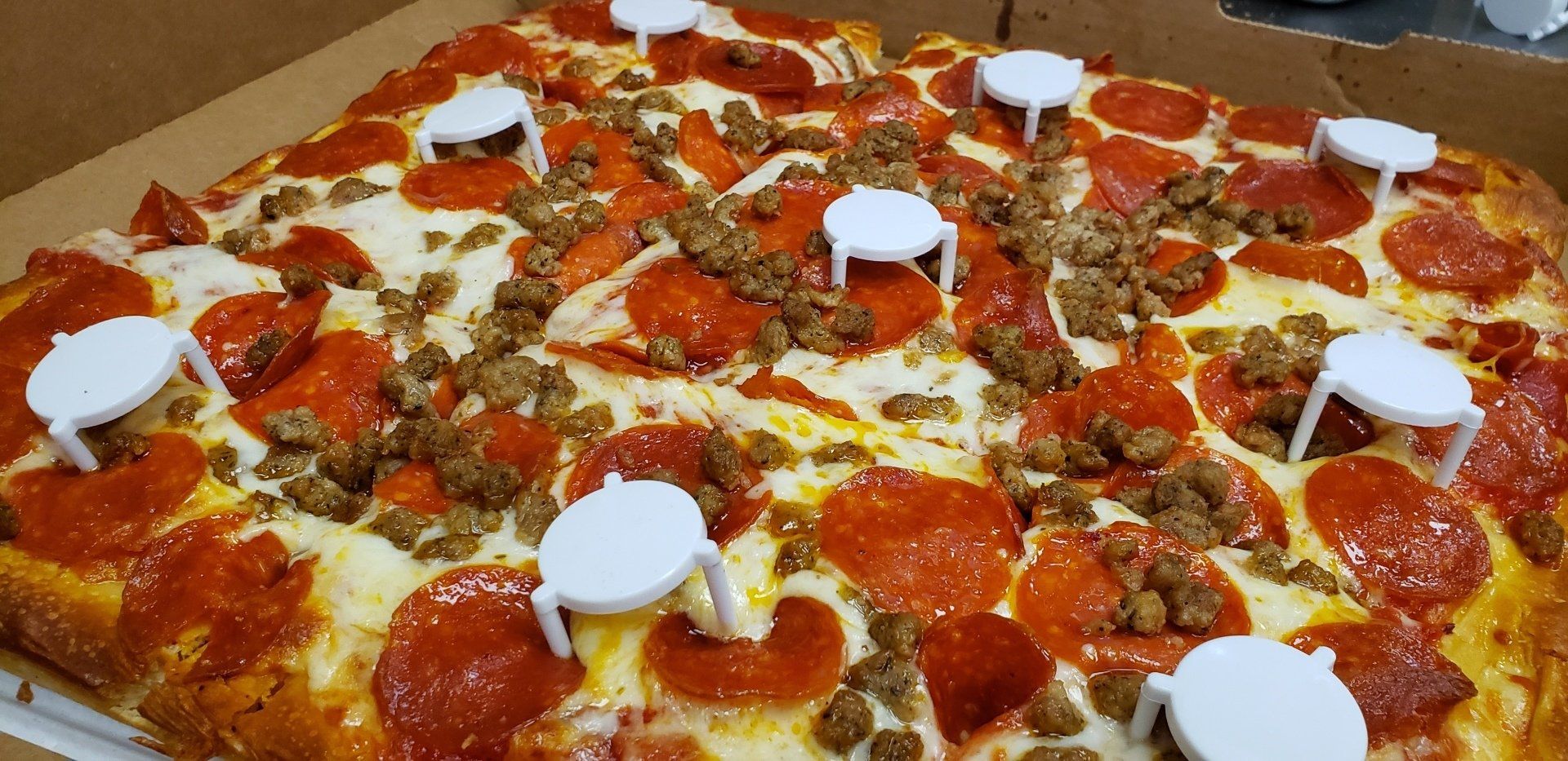 A pizza with pepperoni and sausage on it is in a box.