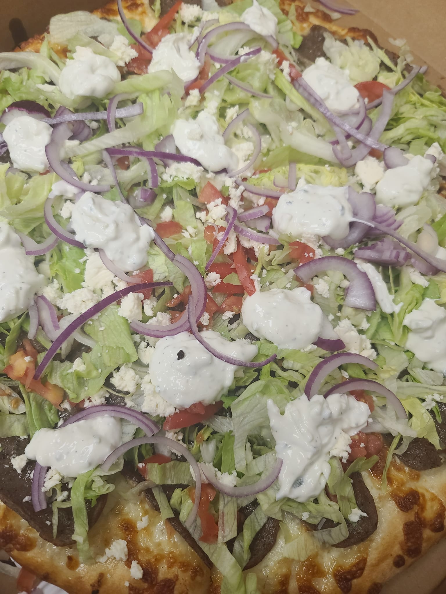 A pizza with lettuce , onions , cheese and ranch dressing on it.