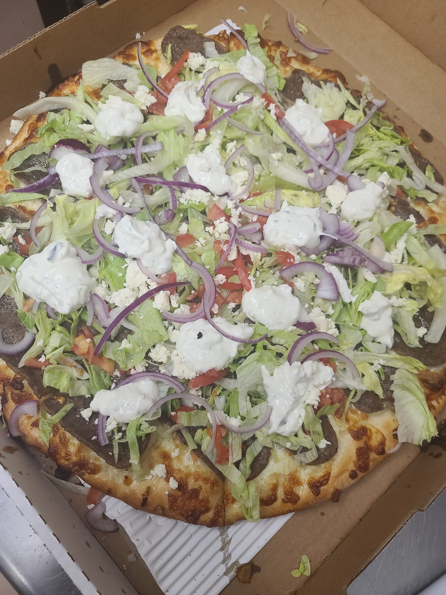 A pizza with lettuce , cheese , onions and tomatoes is in a box.