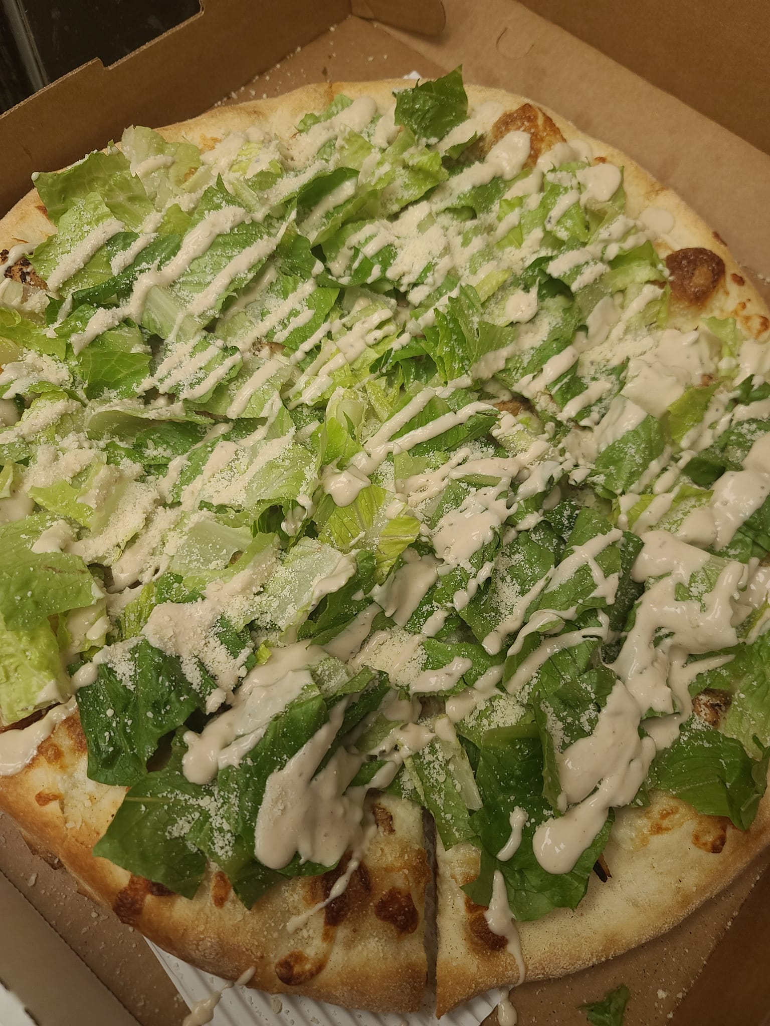 A pizza with lettuce and sauce on it is in a box.