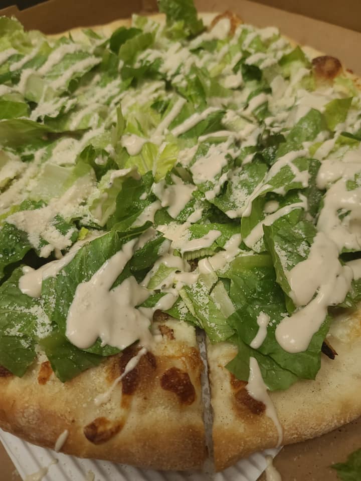 A pizza with lettuce and ranch dressing is in a box.
