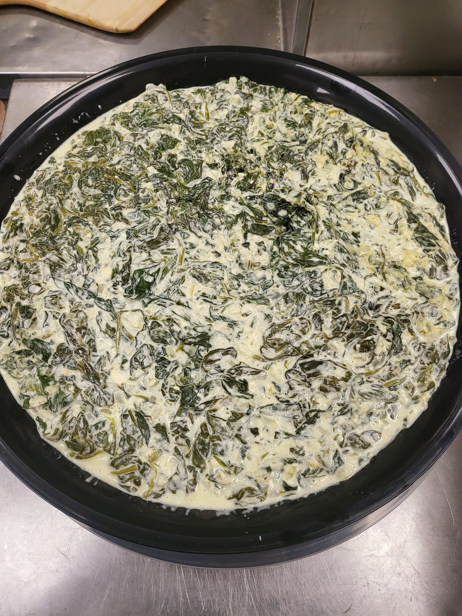 A pizza with spinach and cheese in a pan on a table.