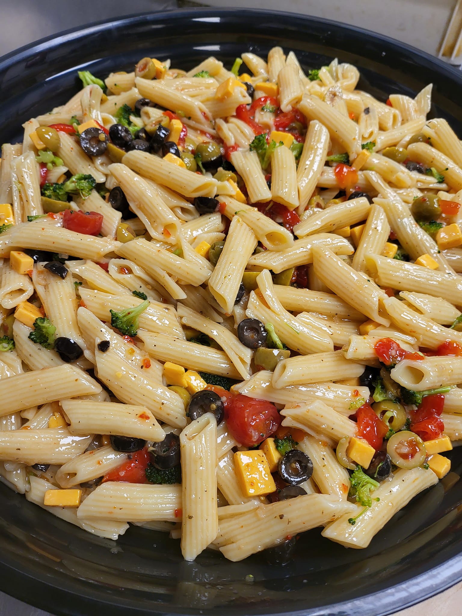 A pasta salad with tomatoes , broccoli , corn , olives and cheese on a black plate.