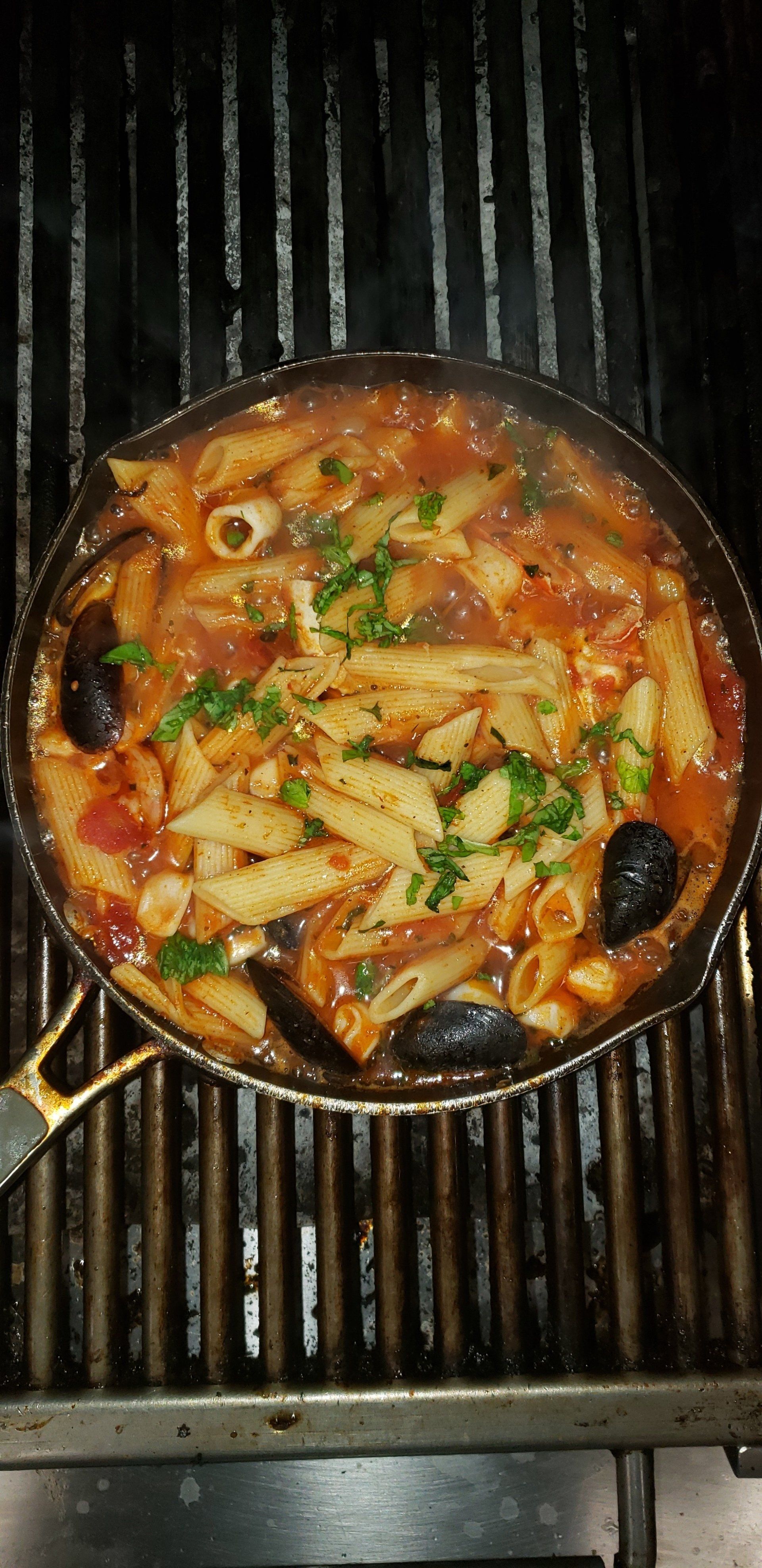 A pan of pasta and seafood is cooking on a grill.