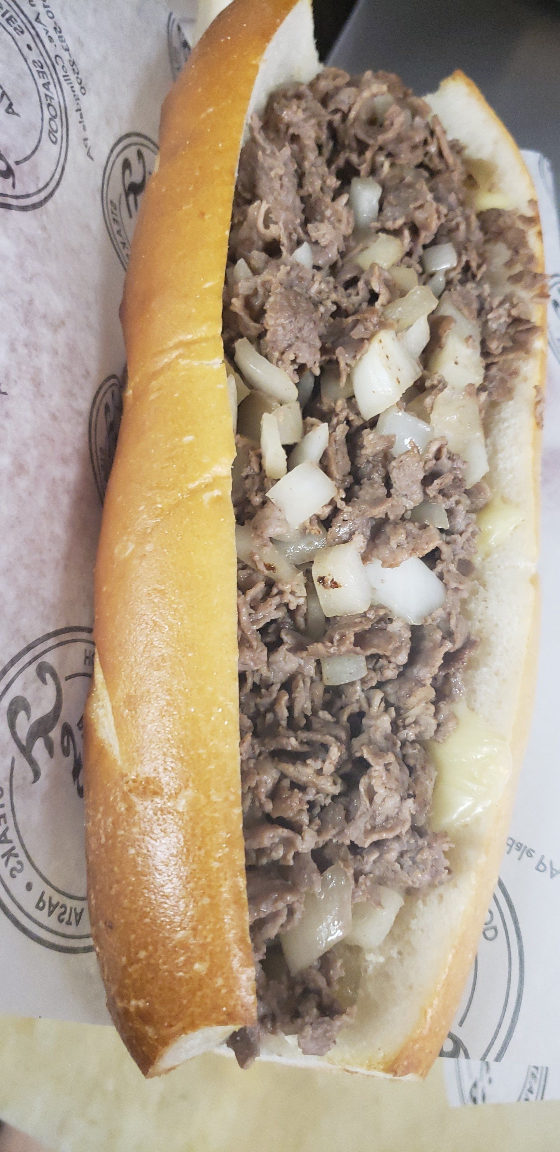 A close up of a steak sandwich with onions on a bun on a table.