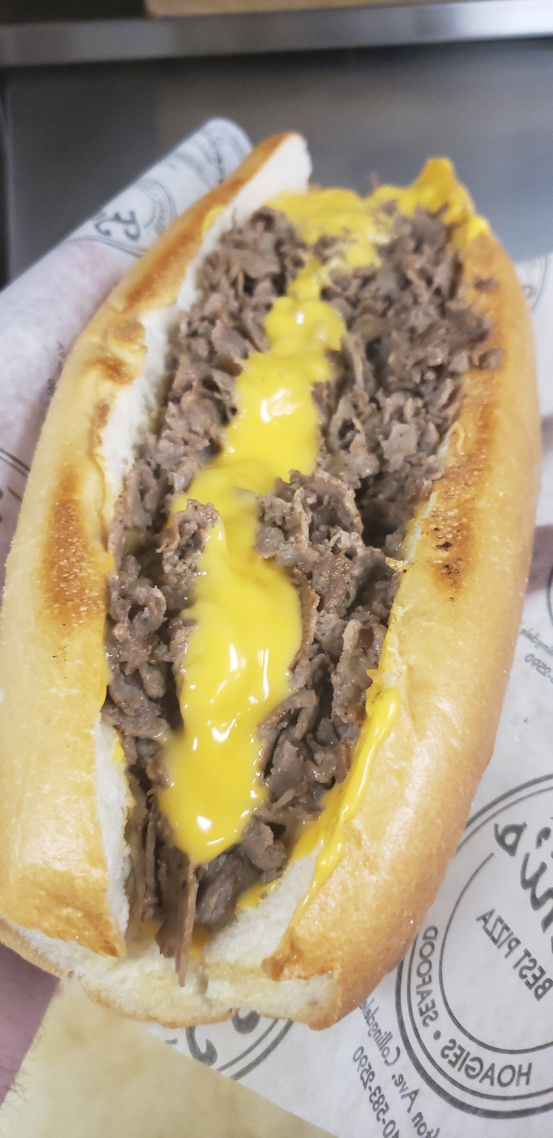A close up of a steak sandwich with cheese on a bun.