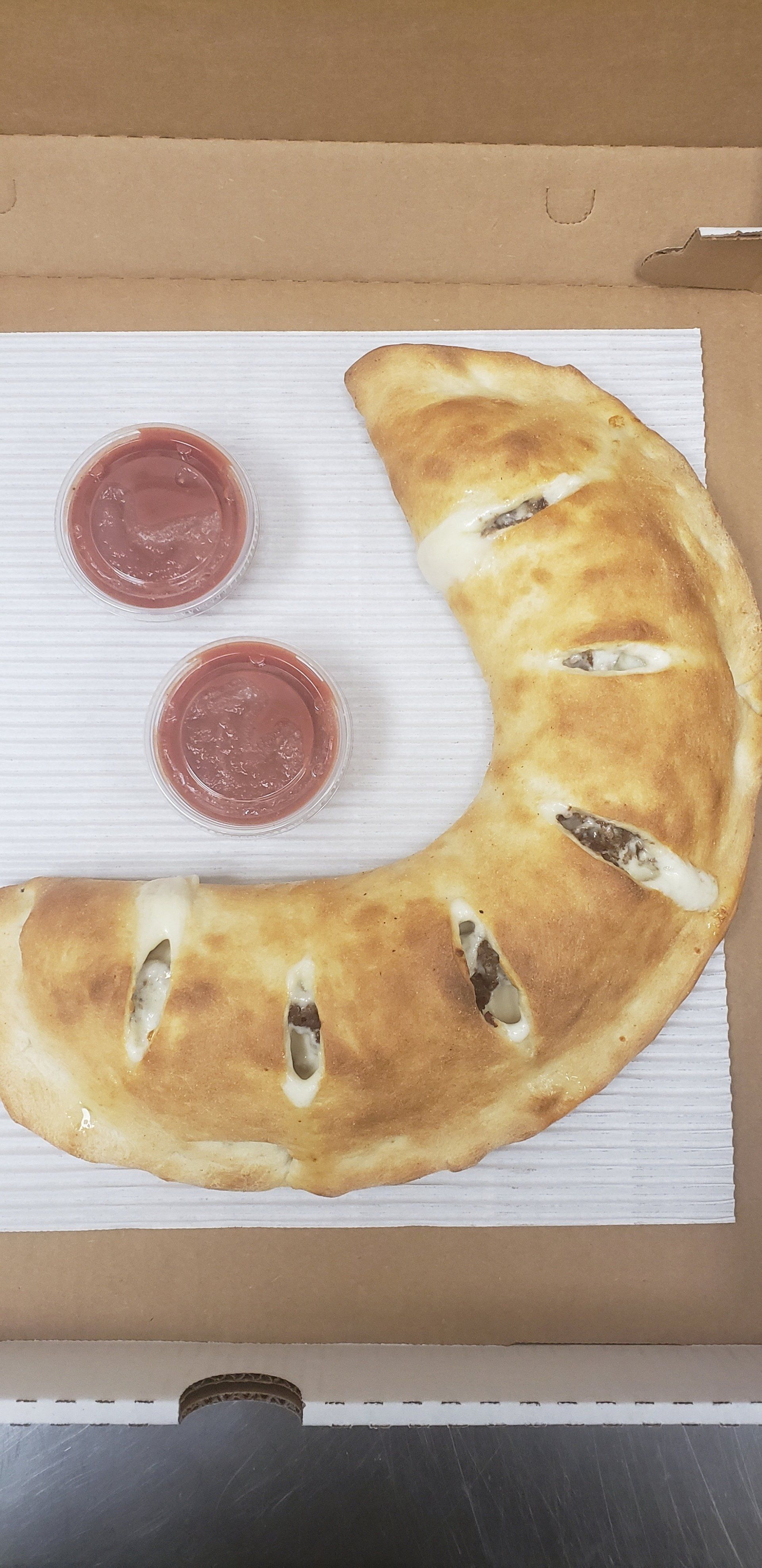 A pizza in a box with two dipping sauces next to it.