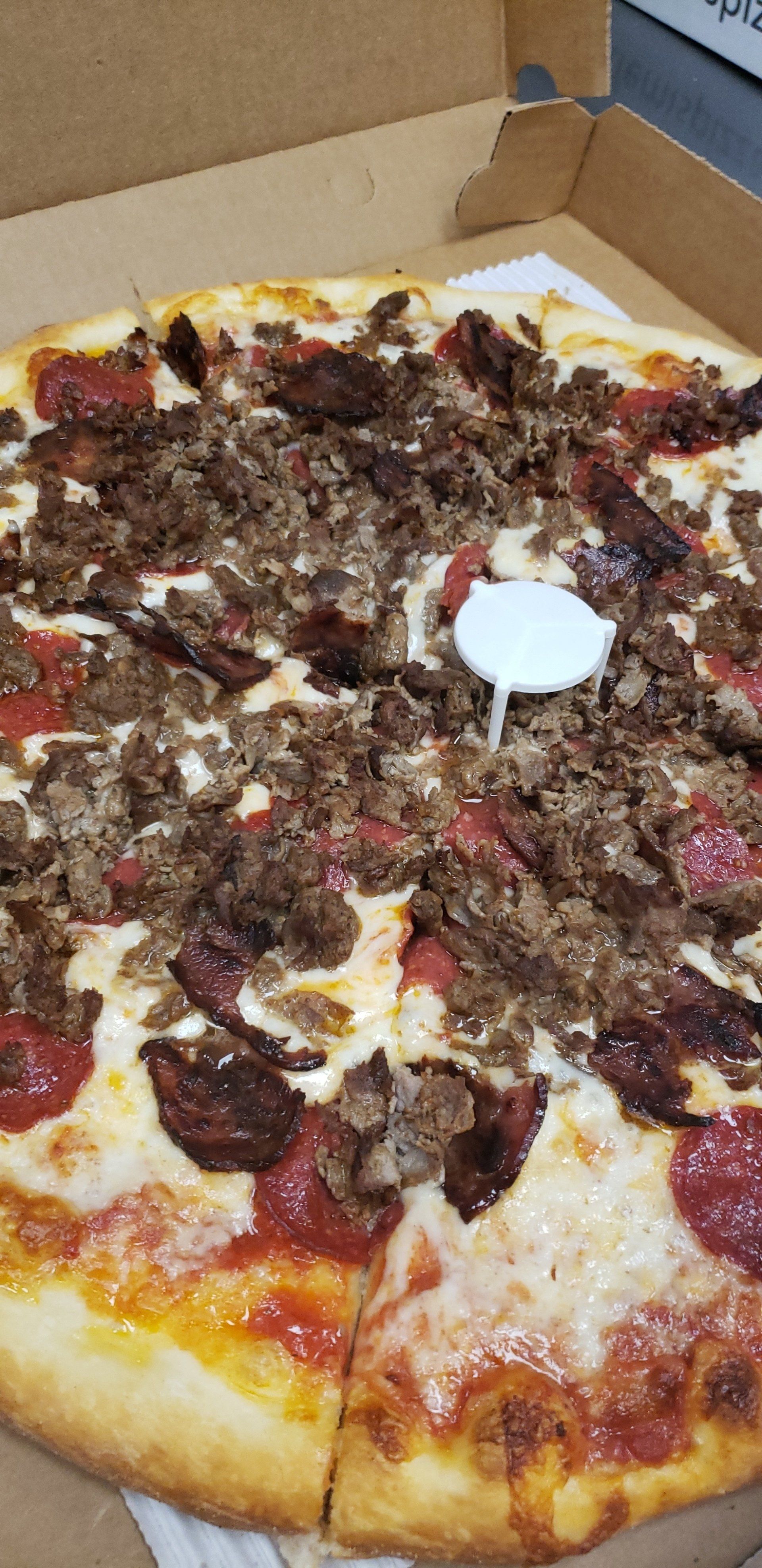 A pizza with meat and pepperoni is in a cardboard box.