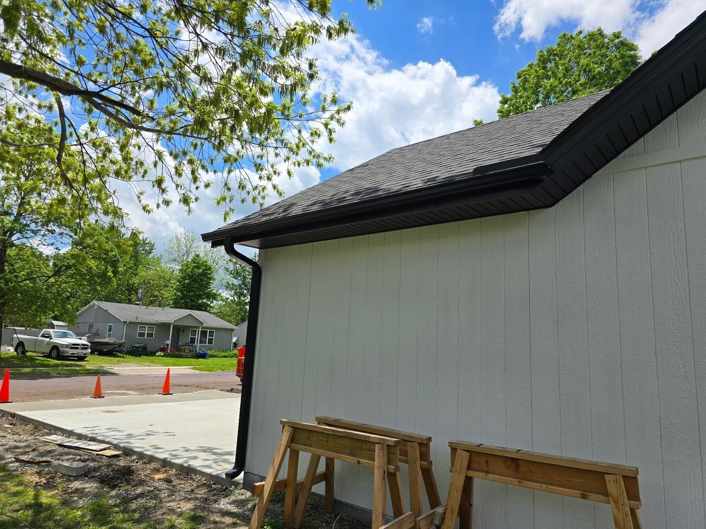 A building with black gutters and trim, white siding, and a gray roof on a sunny day.