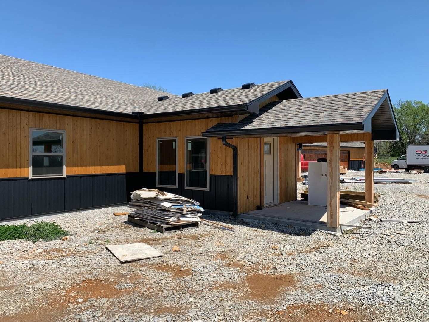 New construction house with brown siding, black trim, and a porch under a clear blue sky.