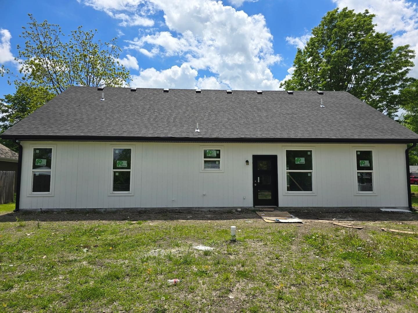 White house with dark roof and windows, surrounded by green grass under a blue sky.