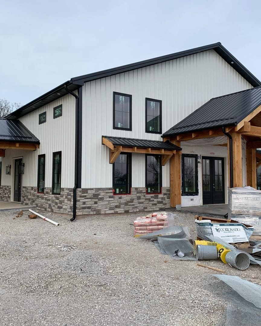 Modern white building with black accents, stone base, and black roof under construction.