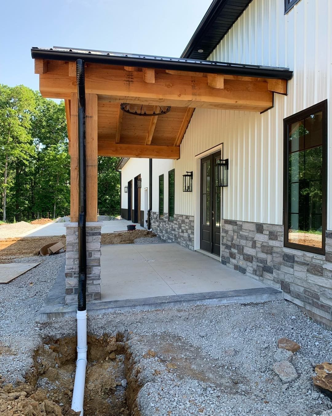 Covered porch with wood beams, gray stone, white siding, and black gutters.
