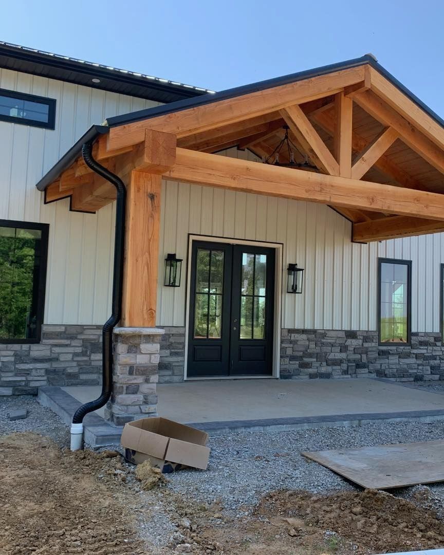 Exterior of a house with stone base and wood-beam covered entrance with black double doors and black trim windows.