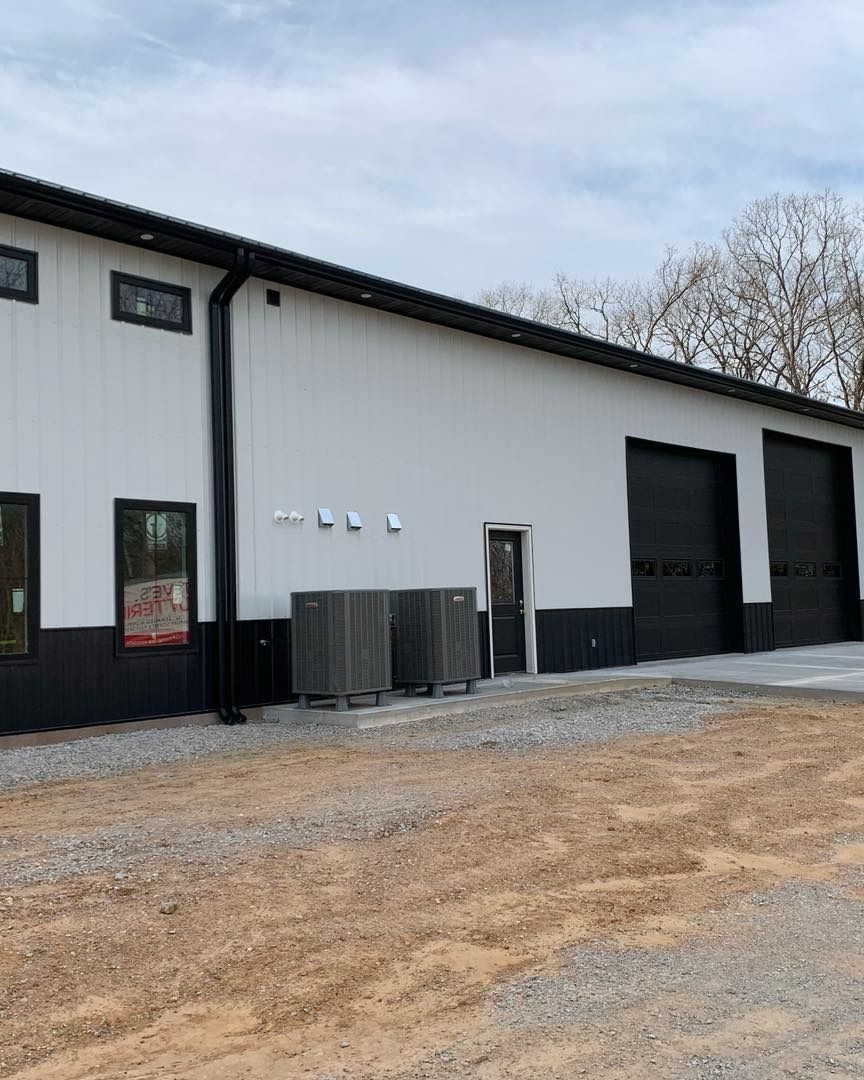White and black commercial building with three garage doors and HVAC units in front.