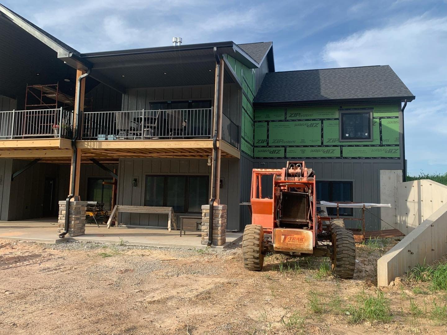 Construction of a two-story house with a balcony. An orange forklift is in the foreground.