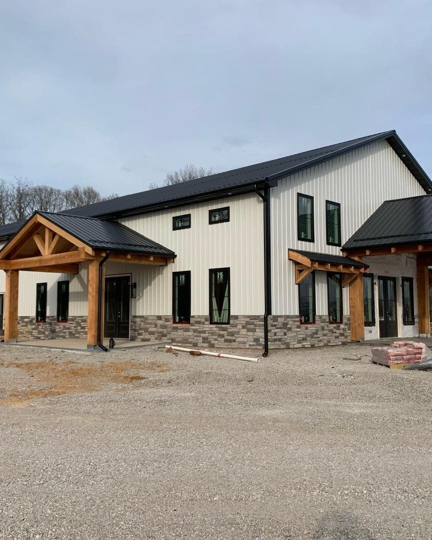 Building with white siding, black roof, stone base, and wooden accents, under construction.