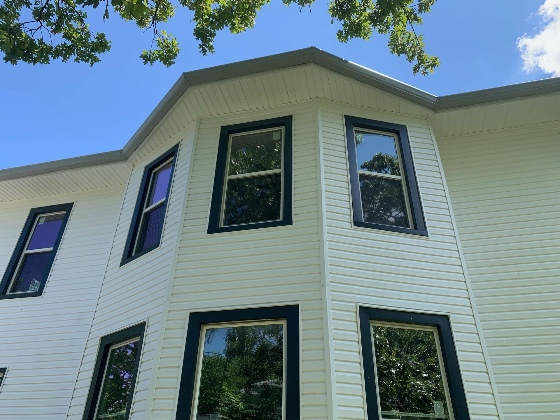 White house with blue-trimmed windows under a blue sky, with some tree branches overhead.