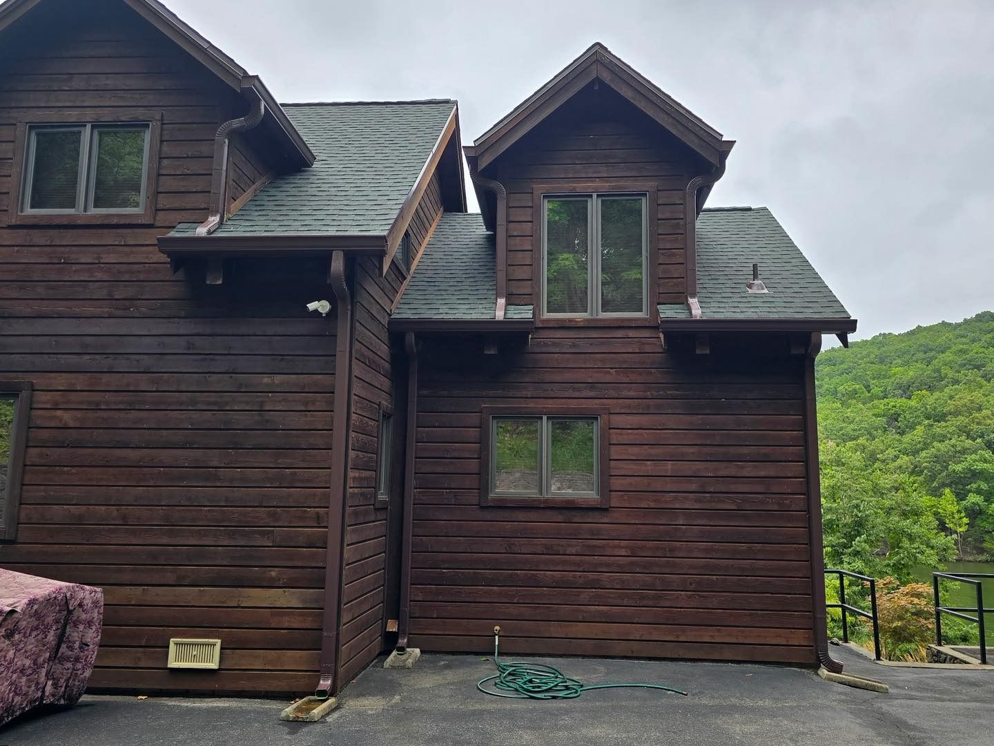 Dark brown wooden cabin with multiple windows, surrounded by trees.