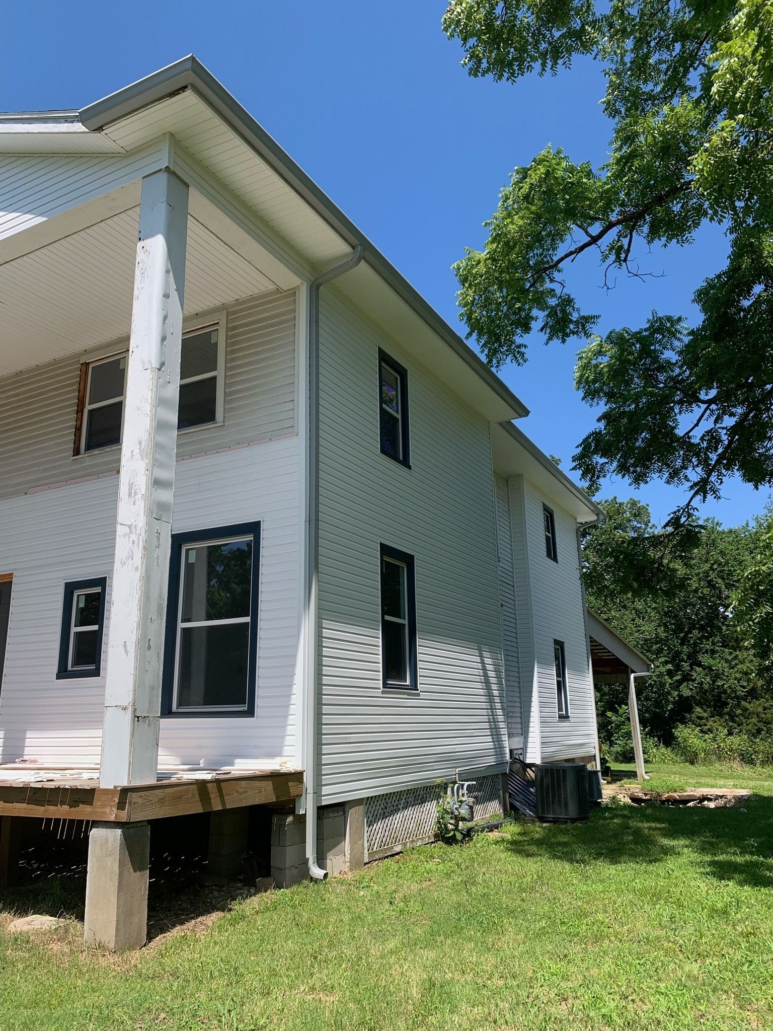 Two-story white house with dark window frames, surrounded by green grass and a tree, under a blue sky.