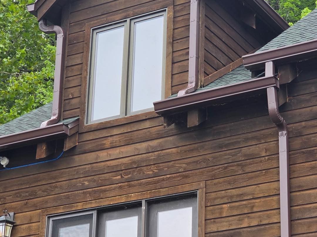 Brown wooden house with two windows and dark brown gutters.