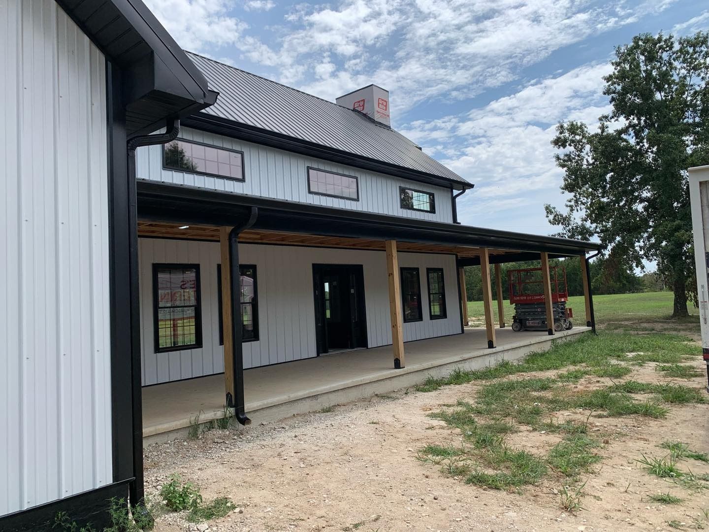 White farmhouse with black trim and a porch under a cloudy sky.