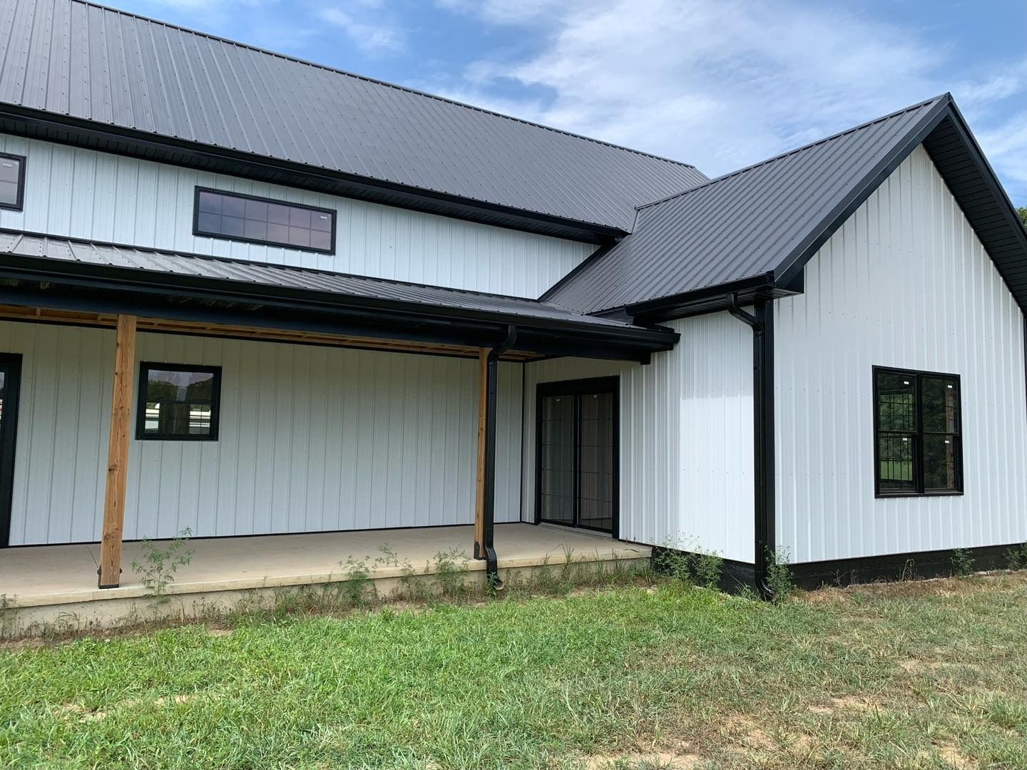 White farmhouse with black trim, metal roof, and porch. Green grass and blue sky.
