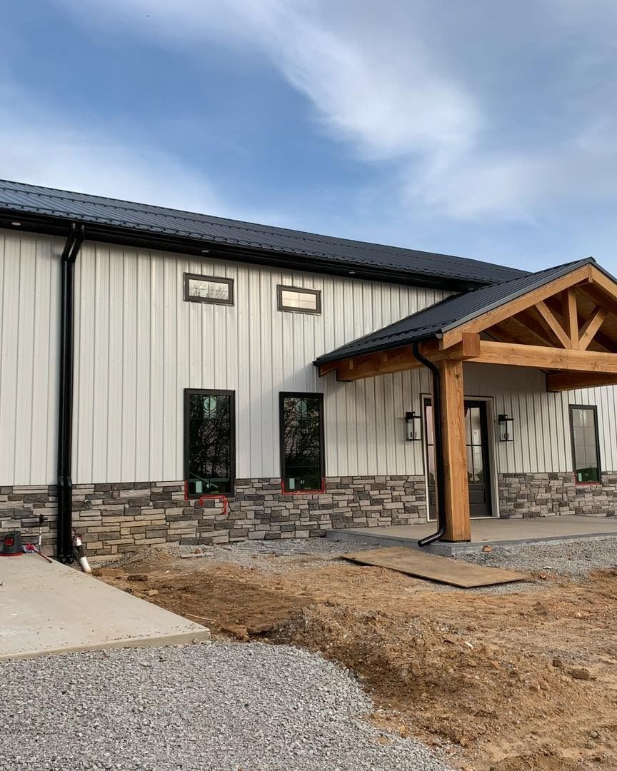 Building exterior with white siding, stone base, and wooden entryway. Black roof and accents under a cloudy sky.