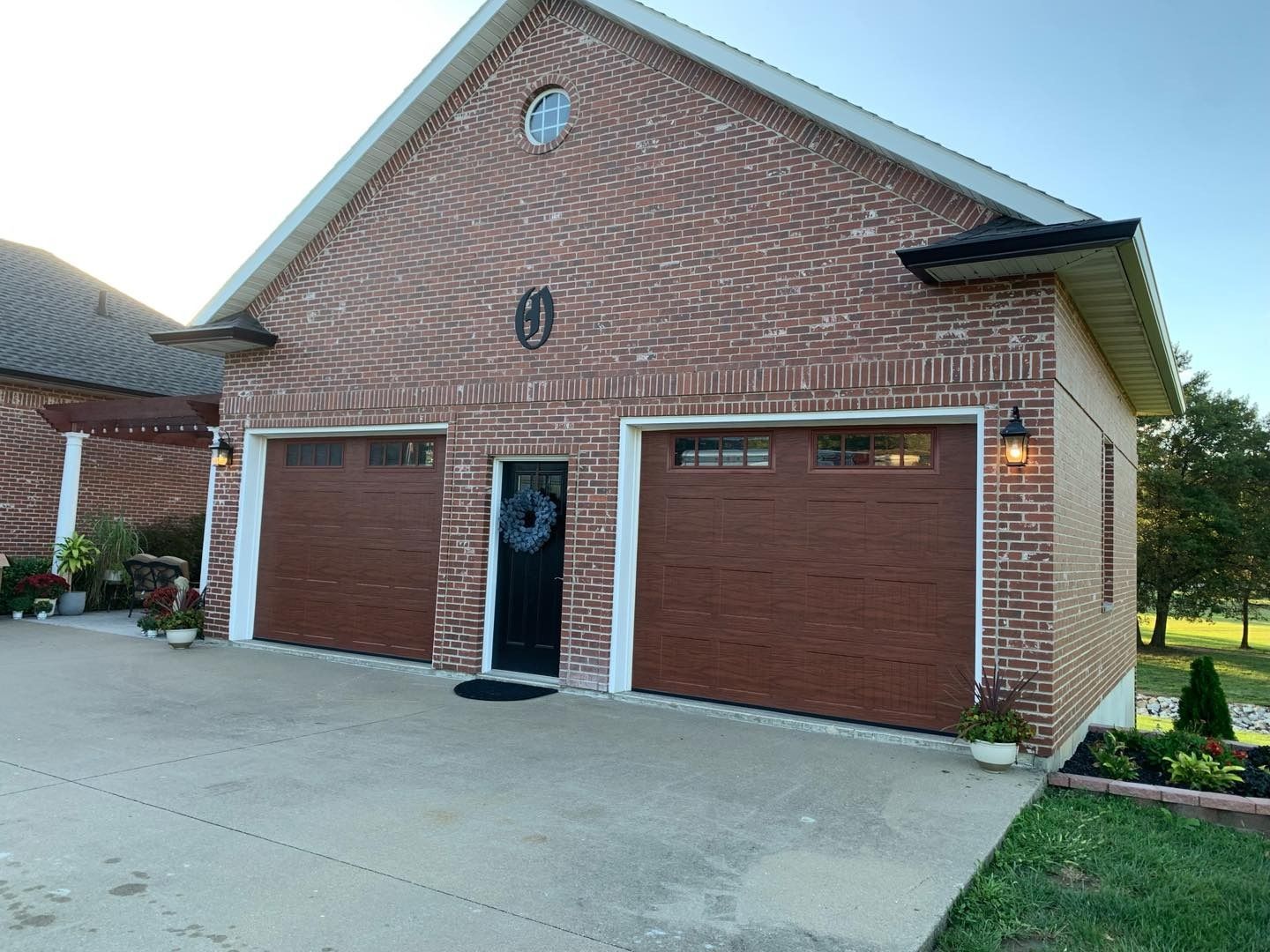 Brick two-car garage with brown doors and a black front door. Exterior features include sconces and landscaping.