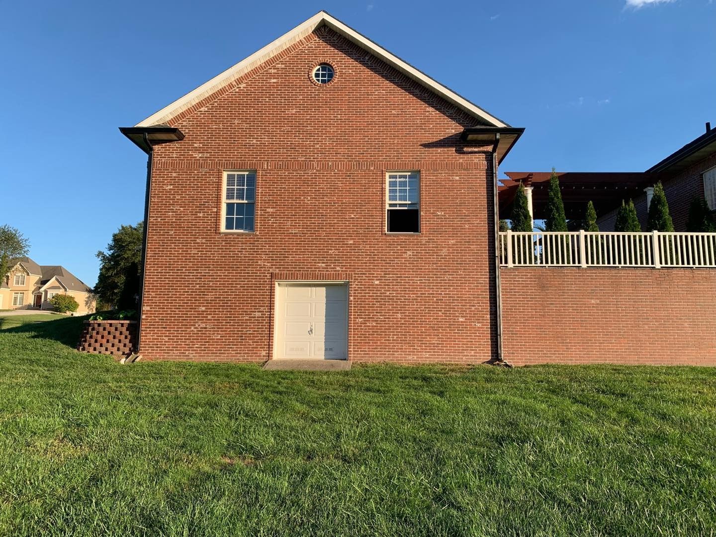 Red brick building with white door, two windows, and grassy yard.