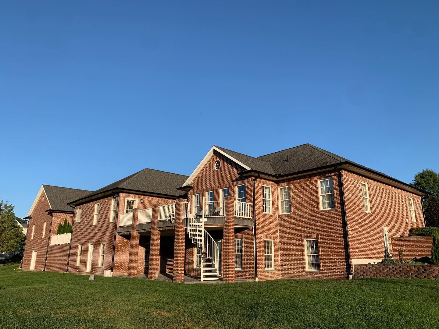 Brick building with multiple levels under a clear blue sky. A grassy lawn is in the foreground.