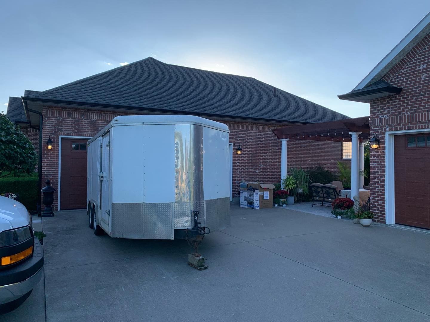 White trailer parked in front of a brick garage and house, under a cloudy sky.