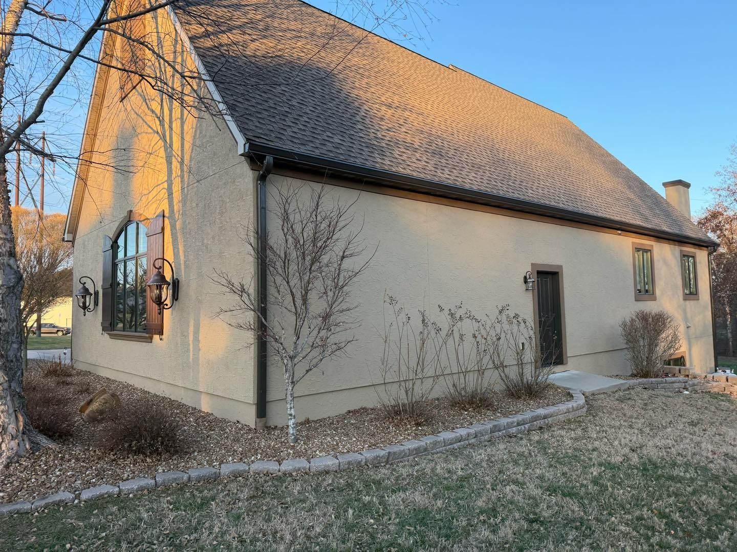 Beige stucco building with a steeply pitched tile roof; a single arched window is on the left.