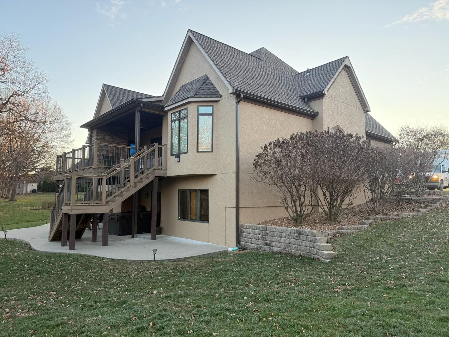 Tan stucco house with a wooden deck and steps in a grassy yard.
