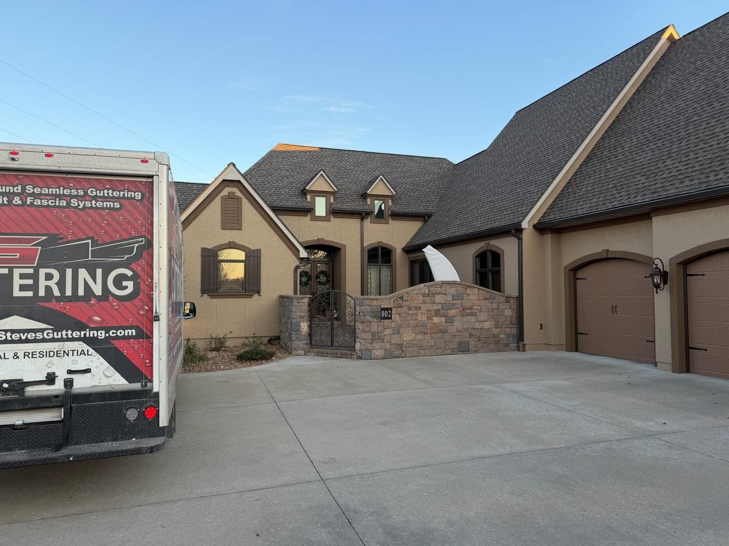 A delivery truck parked in front of a tan stucco house with a brown roof and garage.