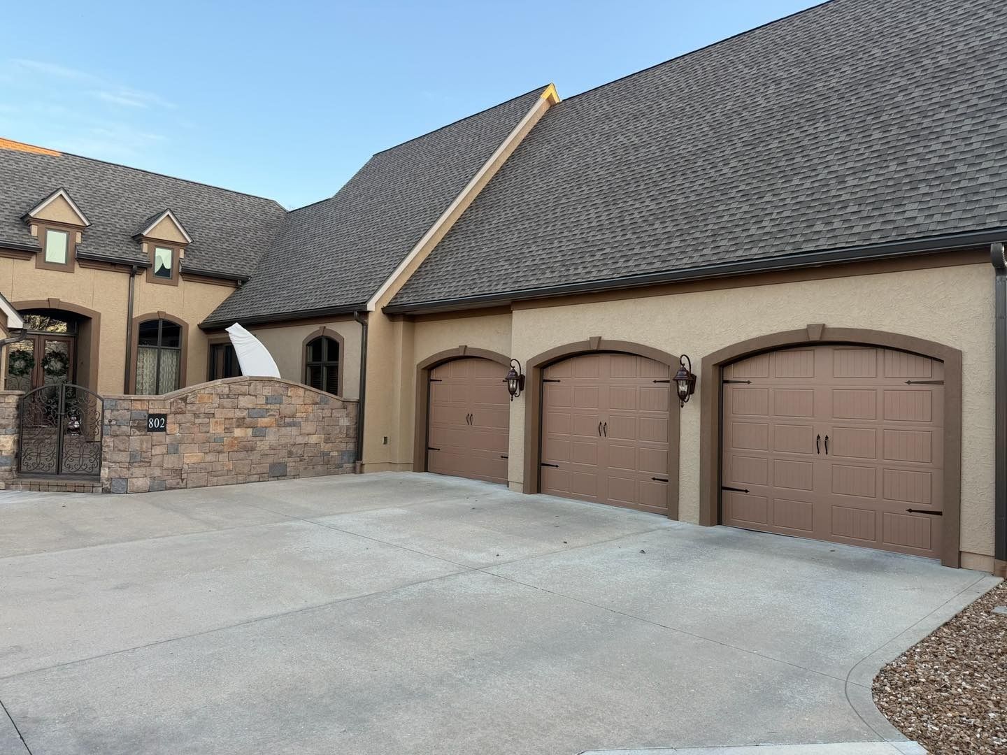 Tan stucco house with three brown garage doors under a dark gray roof.