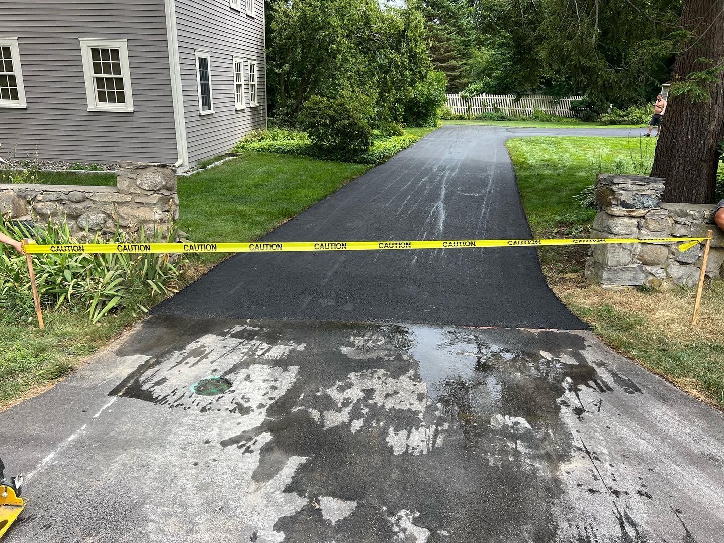 Freshly paved asphalt driveway with caution tape, partially wet.