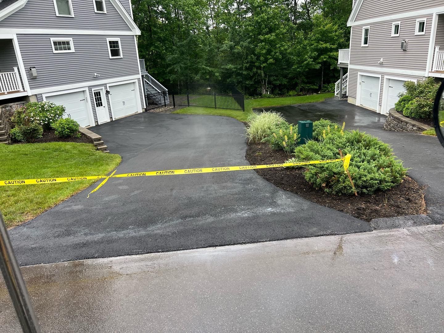 Two attached gray houses with driveways, blacktop, landscaping, and yellow caution tape.