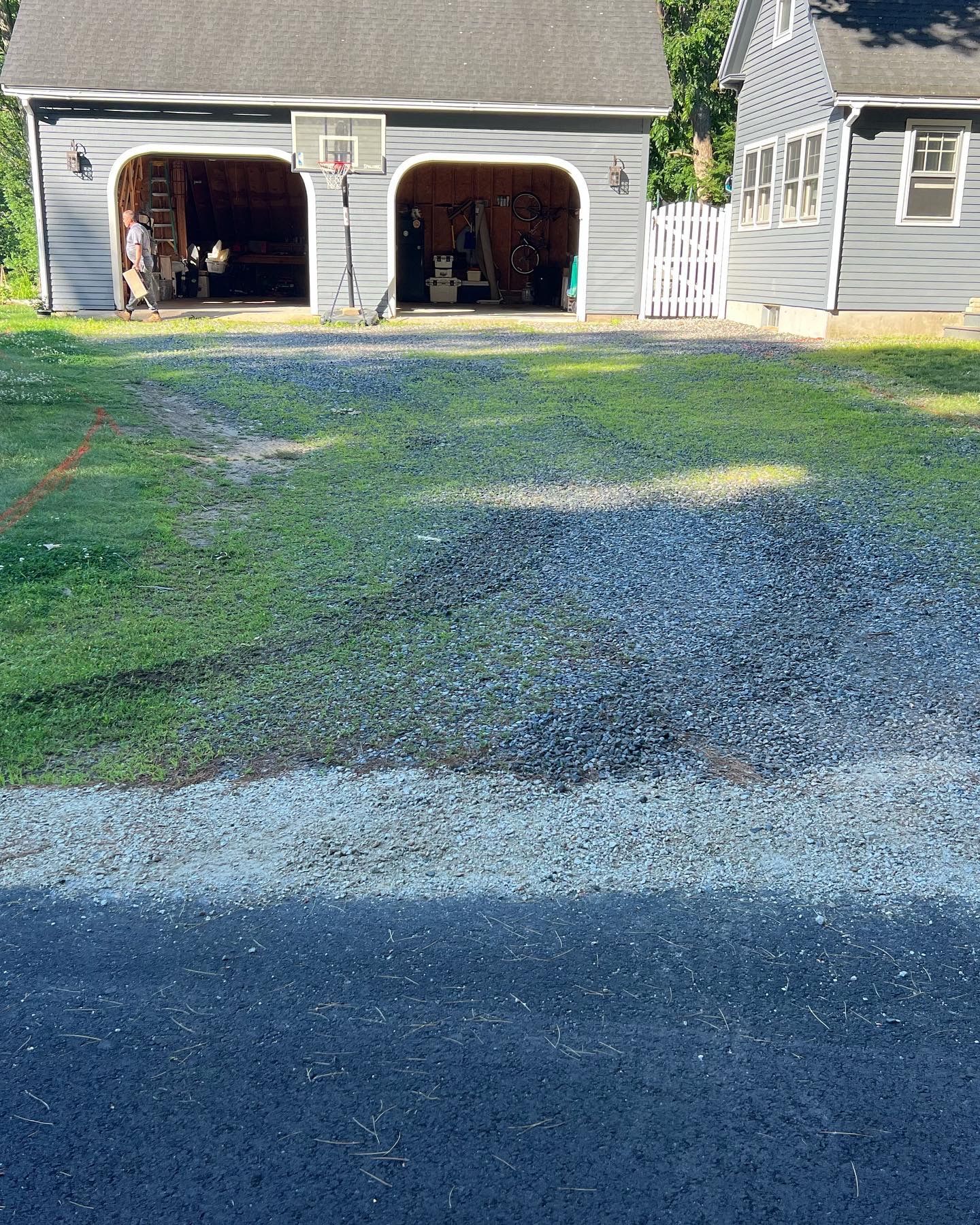Gravel driveway leading to a two-car garage with open doors; a house is to the right.