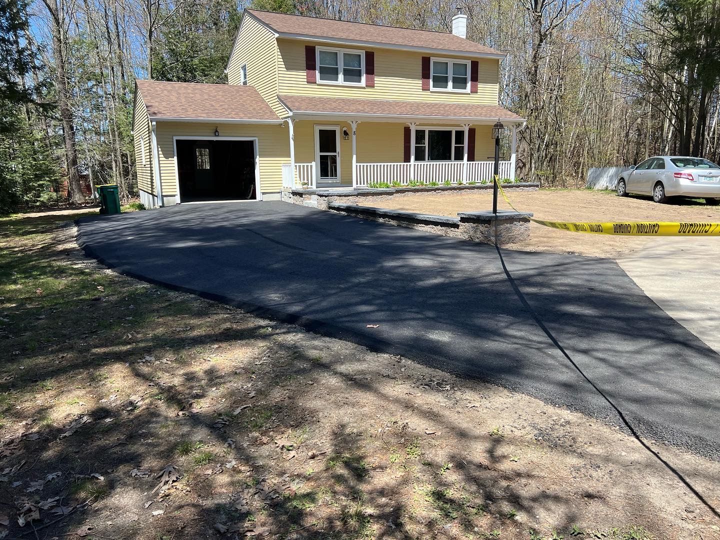 Yellow house with a newly paved driveway. A car sits to the right, and caution tape is present.