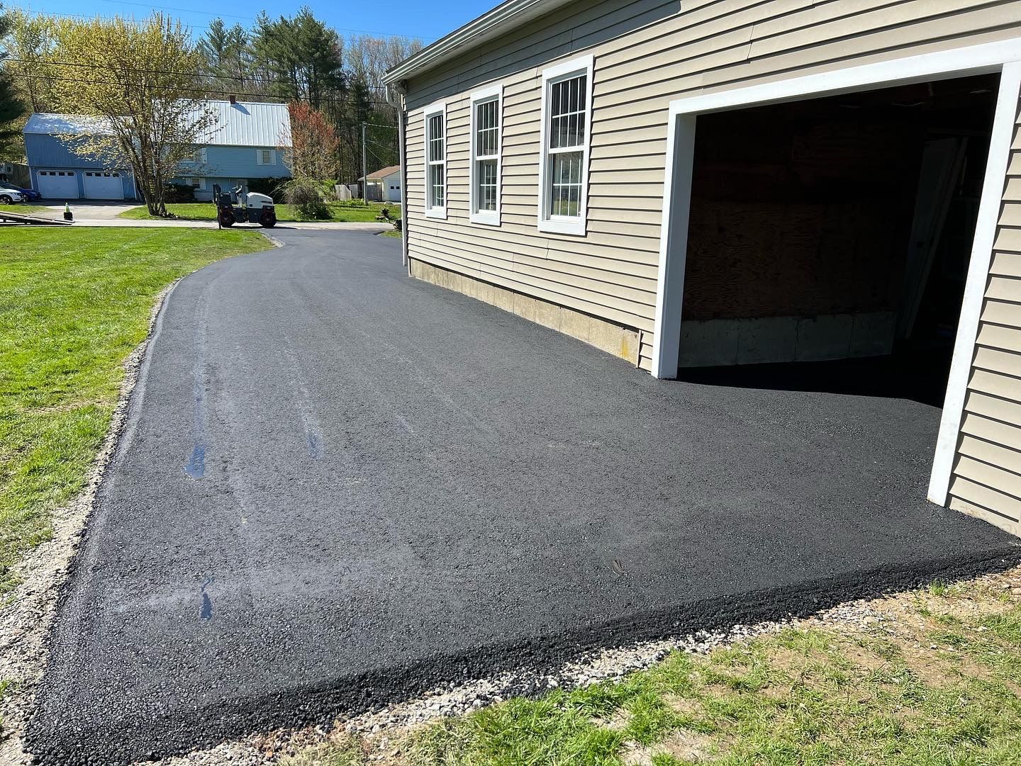 Freshly paved black asphalt driveway next to a light-colored building with an open garage.