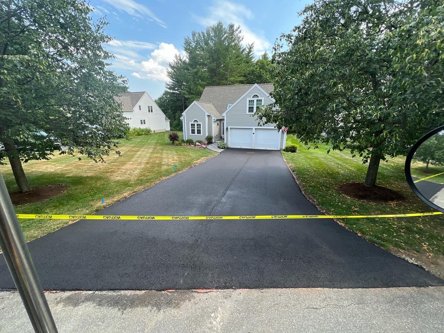 New asphalt driveway in front of a gray house, with caution tape across the foreground.