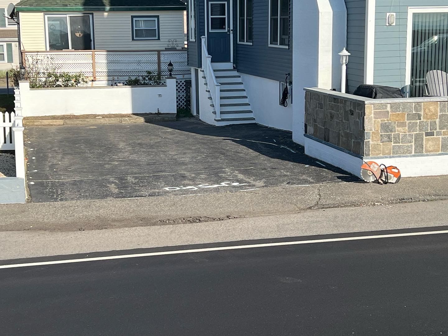 Driveway in front of blue house with stairs. Bike on side of building near street.