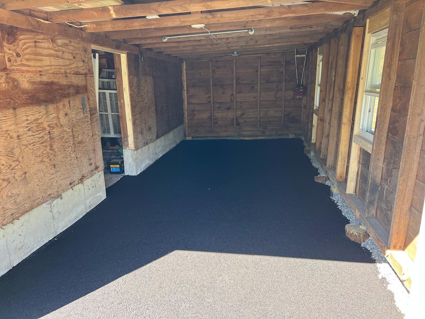 Interior of a garage with a new black asphalt floor. Walls are wood and plastered.