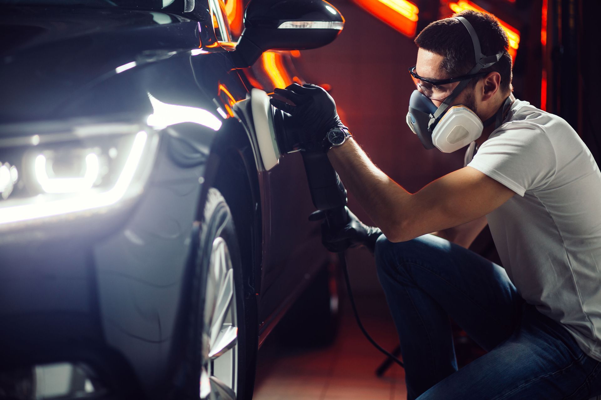 Person polishing a car with a machine, wearing protective gear.