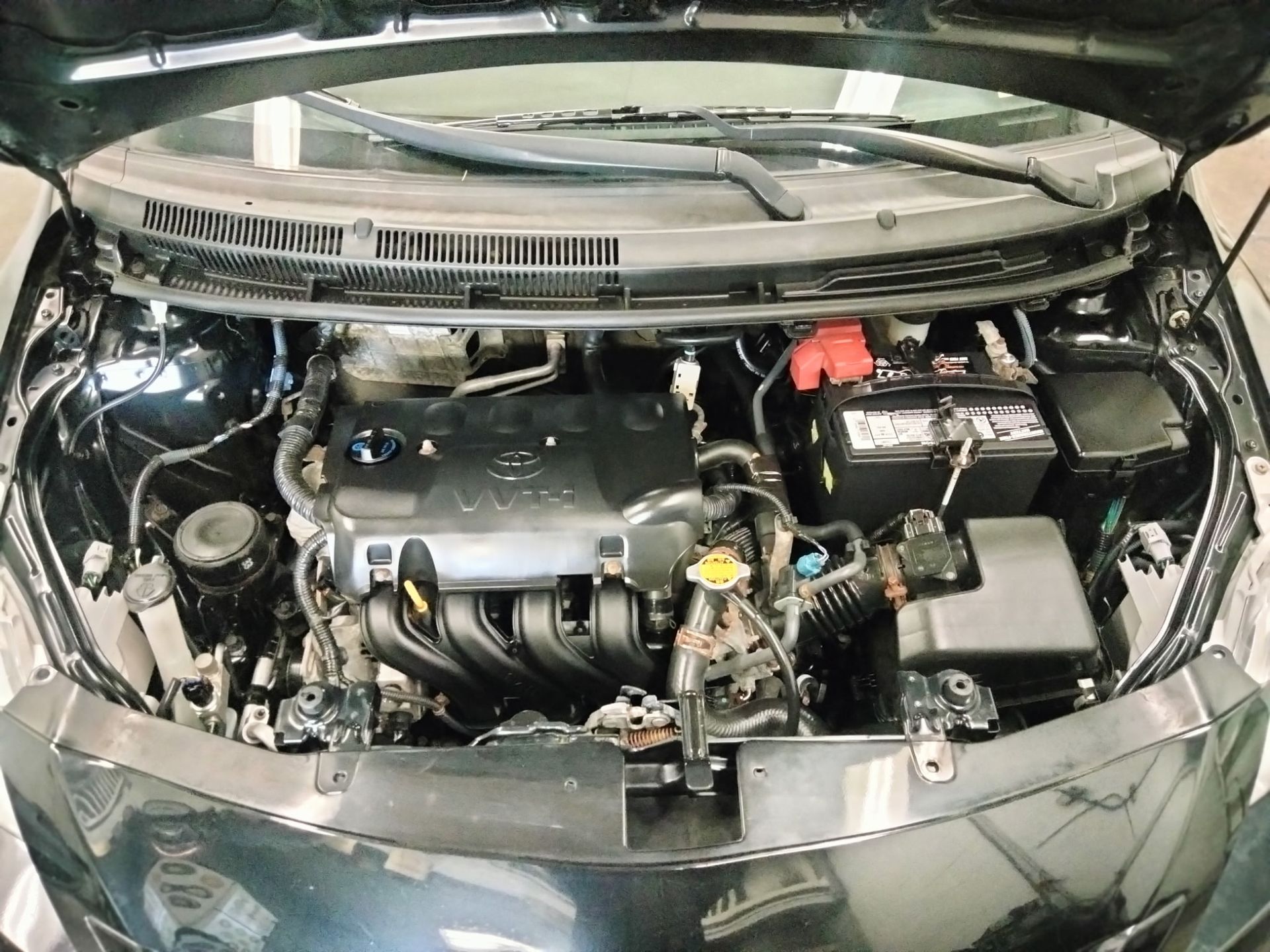Open hood of a black car showing the engine bay and a battery on the right side.