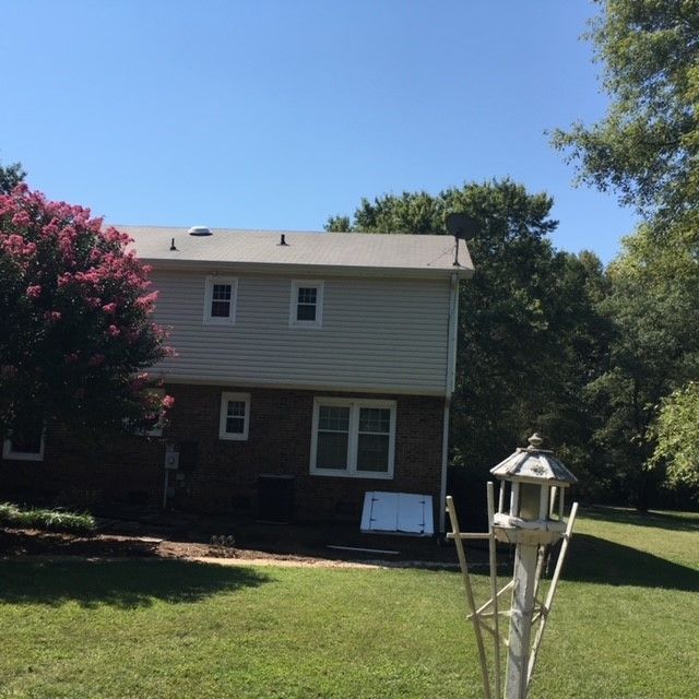 A brick house with a white siding sits in a lush green yard