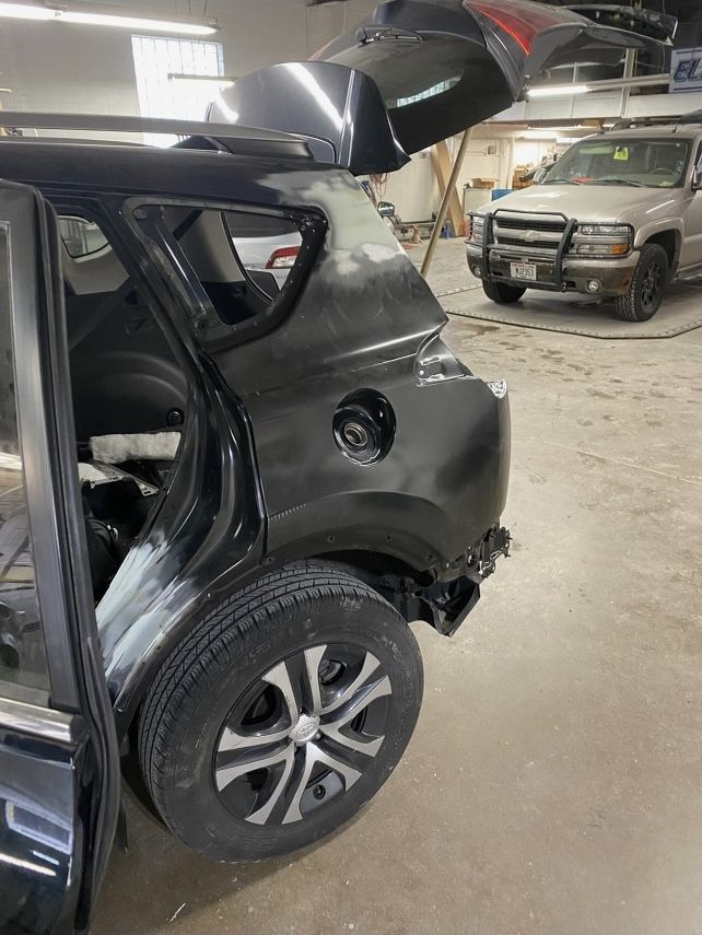 Black SUV in a repair shop, rear quarter panel damage, primed for paint.
