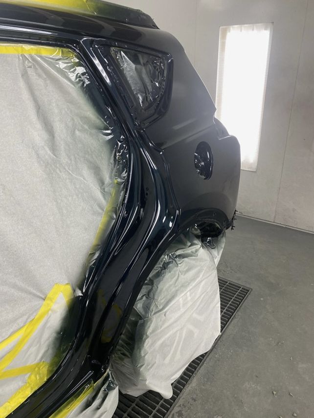 Car rear panel, freshly painted black, masked with plastic, in a paint booth.